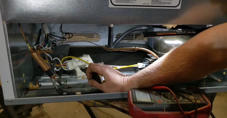 Technician checking compressor wiring and start relay connections on a residential refrigerator