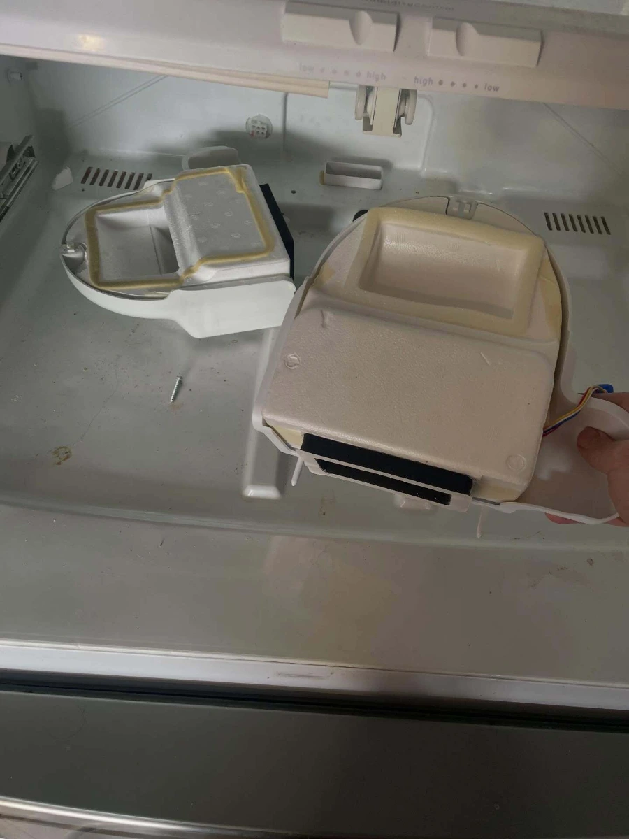 Old and new refrigerator fresh food damper assemblies photographed side by side during a service call
