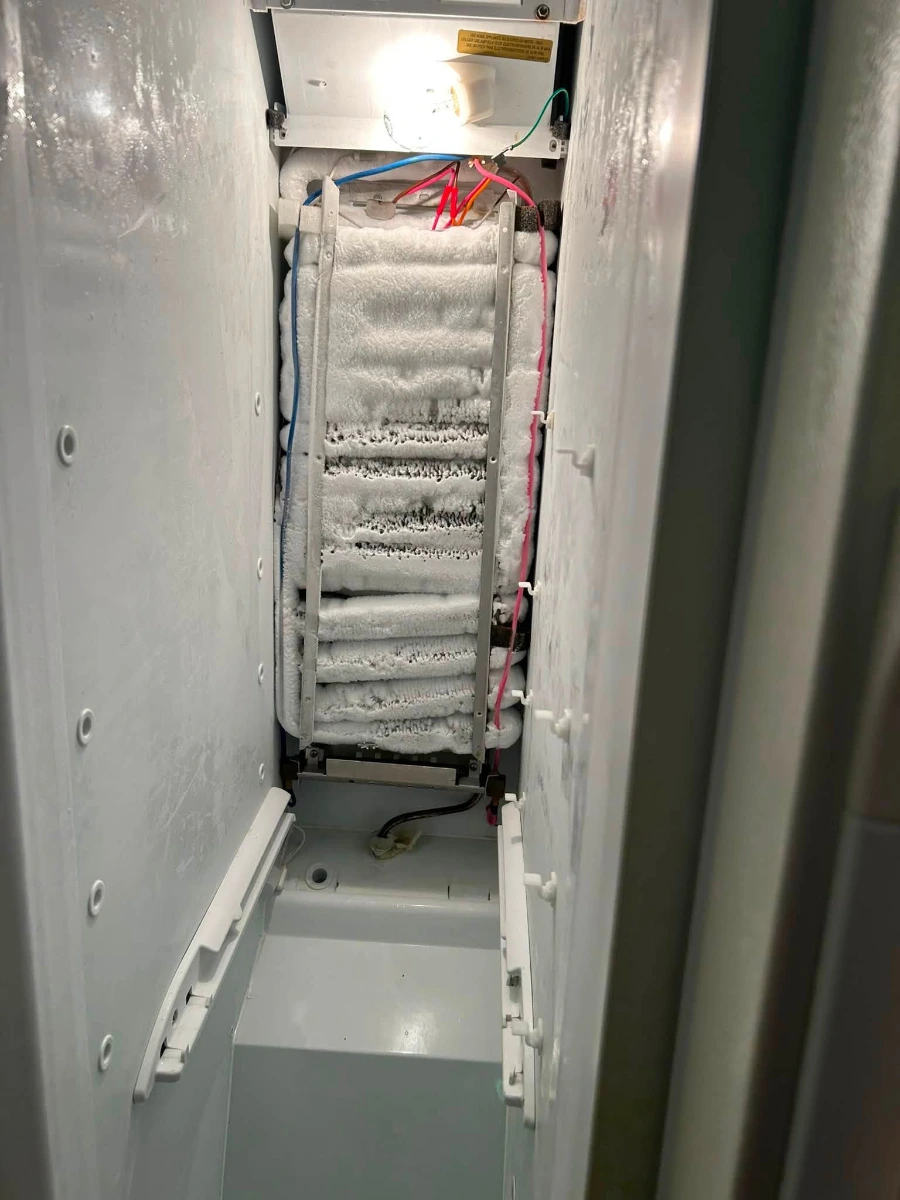 Refrigerator evaporator coil heavily covered in frost and ice during a service inspection